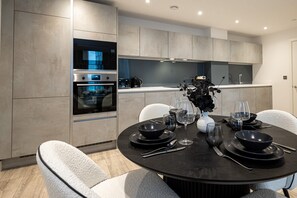 A modern kitchen with built-in appliances, a dining area with a round table set for six, and a view into the adjacent dining room. - Nuvola Suite I Luxury 1BR Apartment I Sky Views (Greater Manchester)