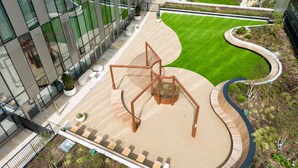 Un bâtiment moderne doté d’une façade en verre, d’une sculpture centrale et d’un jardin aménagé.