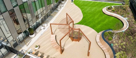 A modern building with a glass facade, a central sculpture, and a landscaped garden area.