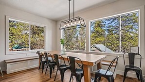 En matplats med ett träbord, svarta stolar och en hänglampa. Stora fönster ger utsikt över träd och ett hus.