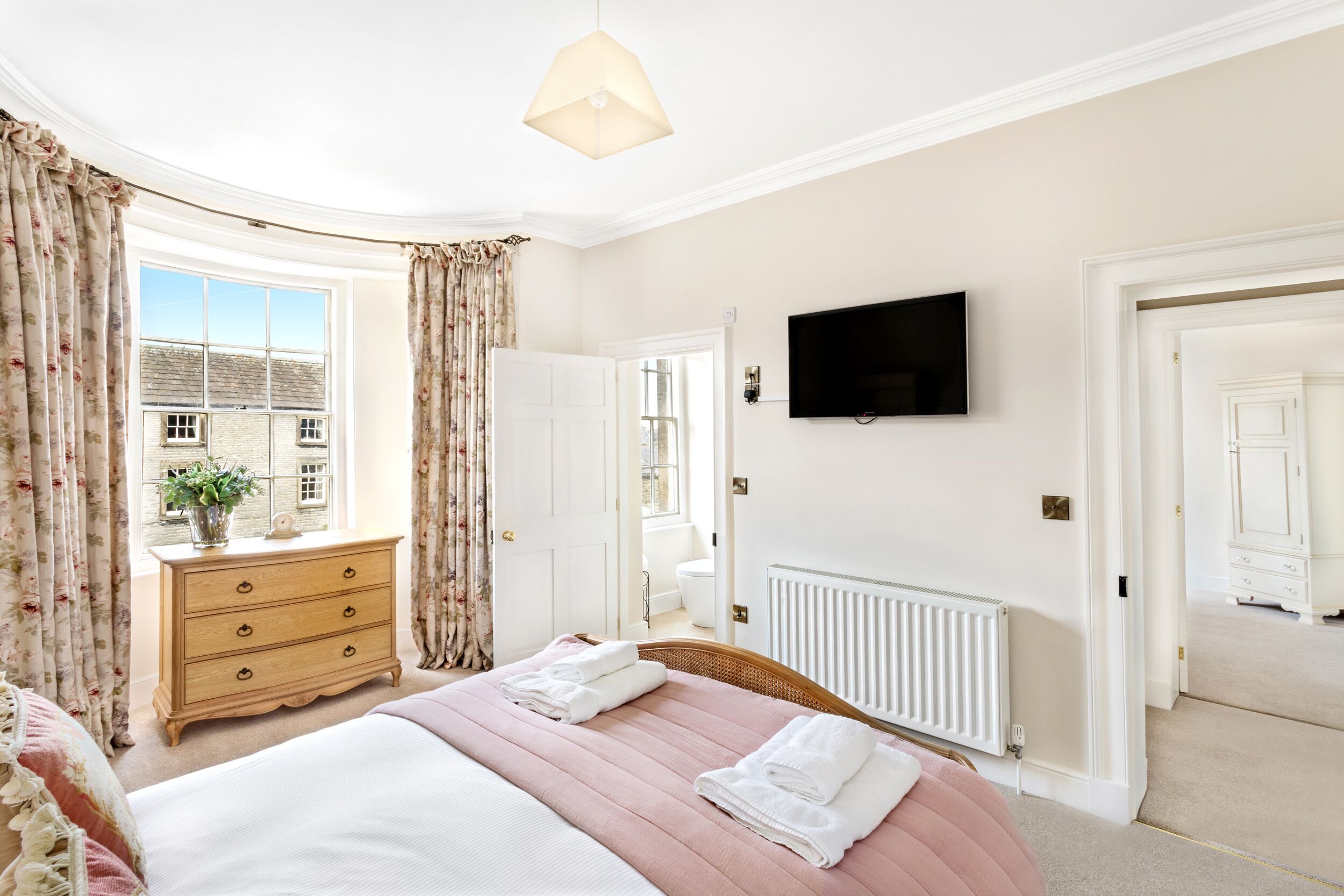 A bedroom with a large bed, a dresser, a TV mounted on the wall, and a window with curtains.