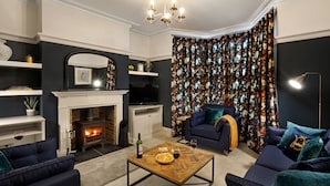 Ein Wohnzimmer mit Kamin, dunkelblauen Sofas, einem Couchtisch und einem gemusterten Vorhang.