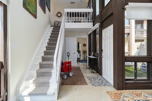 A staircase leading to a second-floor balcony with a railing, a red stroller, and a door with a glass panel. - The Lido Loft | 2-Story Condo, Walk to Lido Beach (Sarasota)
