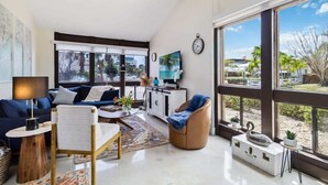 A modern living room with a sofa, armchair, coffee table, and a large window offering a view of the outdoors. - Lido Beach Coastal Escape Near Beach (Sarasota)