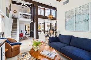 A spacious living area with a blue sofa, a wooden coffee table with decorative items, and a staircase leading to an upper level. - The Lido Loft | 2-Story Condo, Walk to Lido Beach (Sarasota)