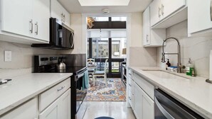 A modern kitchen with white cabinets, a microwave, a kettle, and a sink with a faucet. - Lido Beach Coastal Escape Near Beach (Sarasota)