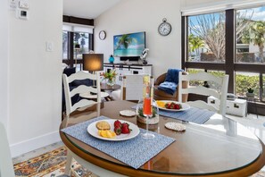 Een eetgedeelte met een glazen tafel, stoelen en ontbijtborden met fruit en een drankje.
