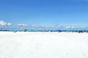 A beach with umbrellas and people, a lifeguard tower, and a clear sky.