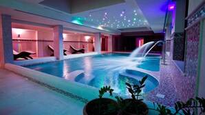A large indoor swimming pool with a water feature, surrounded by seating areas and a tiled floor. - Hotel Relais dei Normanni (Monte Sant'Angelo)
