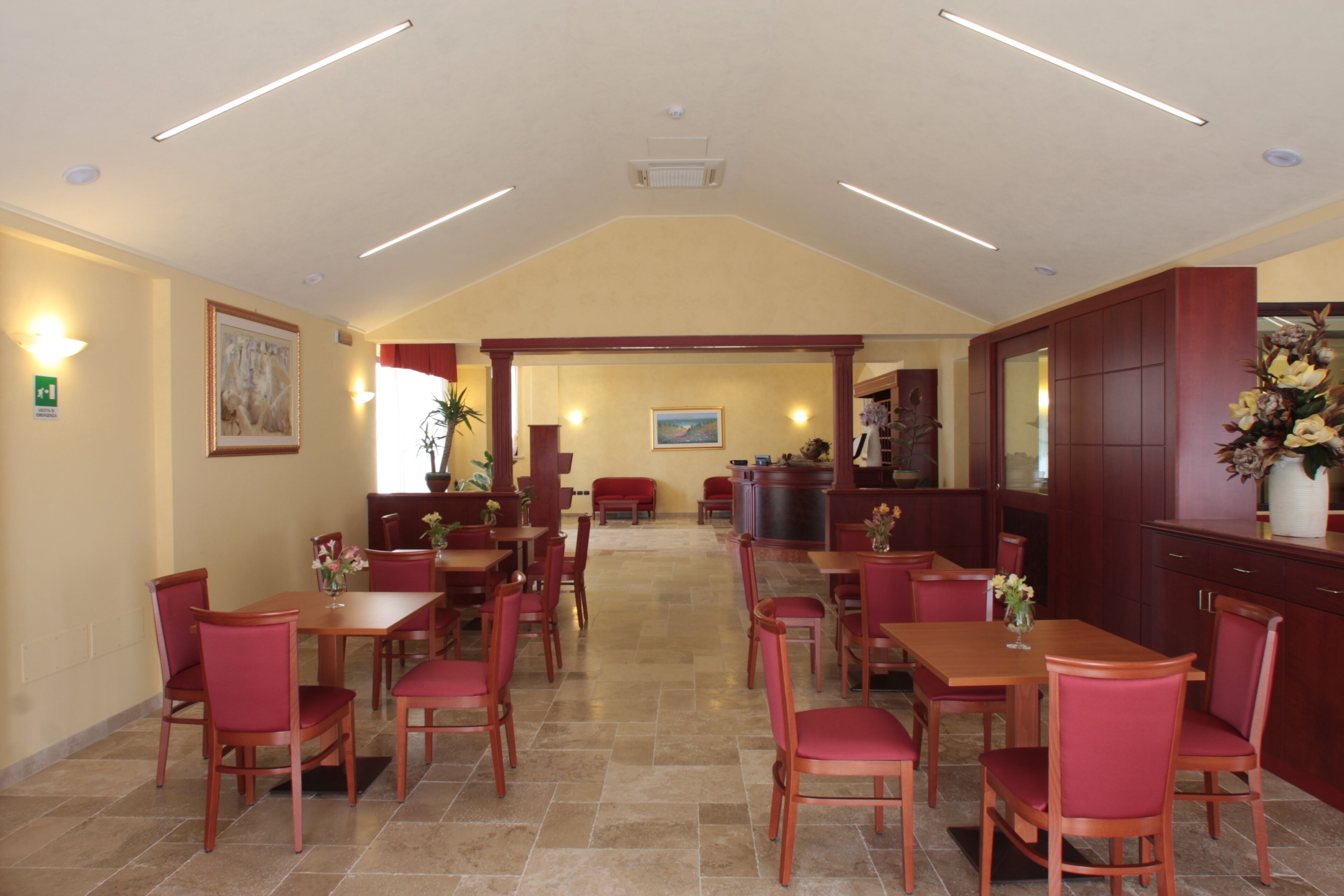 A hotel lobby with multiple dining tables and chairs, a reception area, and a view of the dining area.