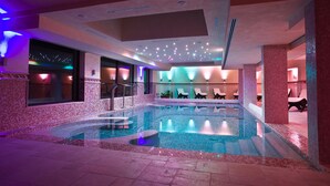 A large indoor swimming pool with a tiled floor and walls, surrounded by lounge chairs and a seating area with a view of the pool. - Hotel Relais dei Normanni (Monte Sant'Angelo)