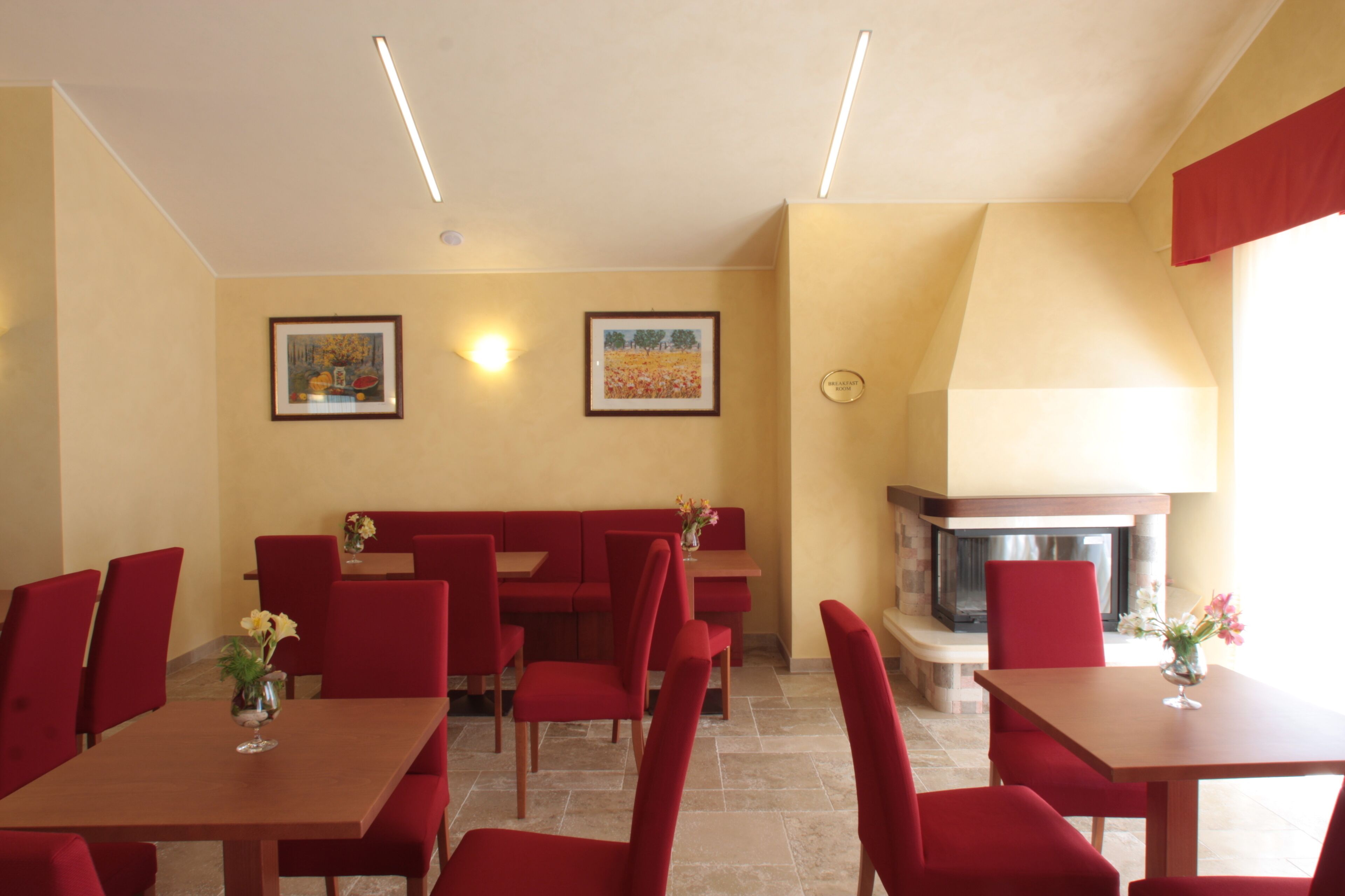 A restaurant with red chairs and tables, a fireplace, and framed artwork on the walls.