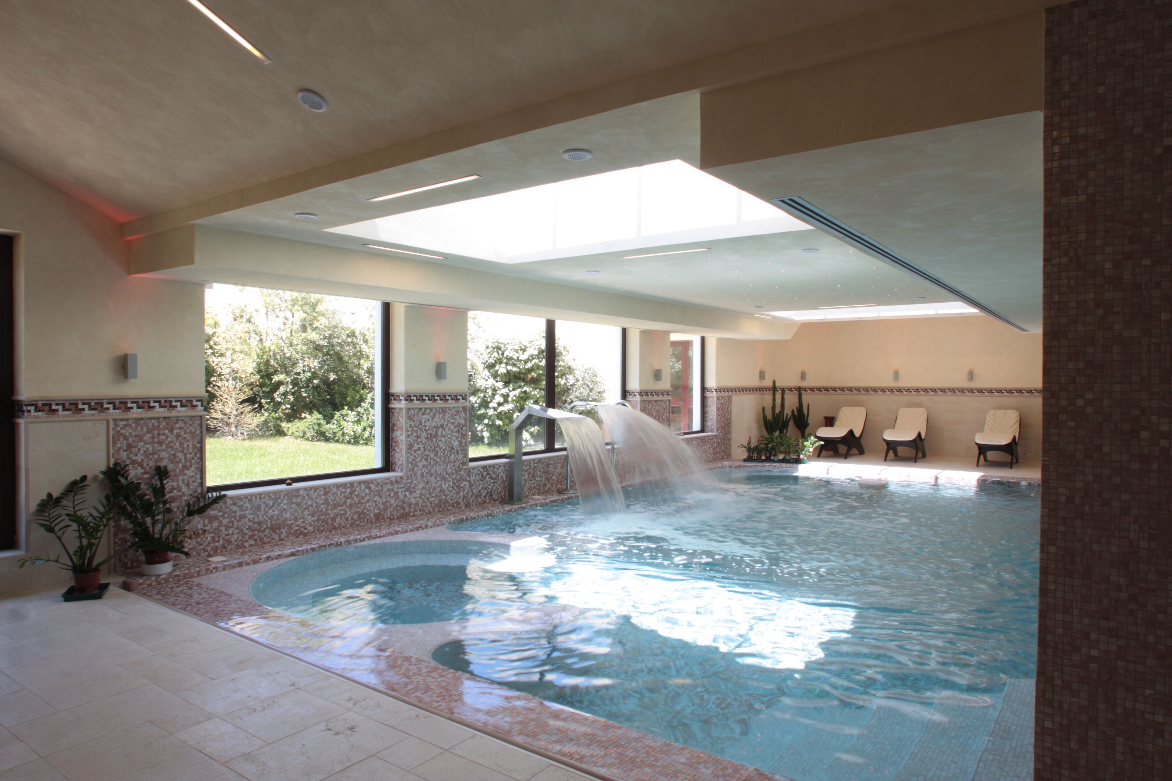 A swimming pool with a waterfall feature, surrounded by lounge chairs and potted plants.