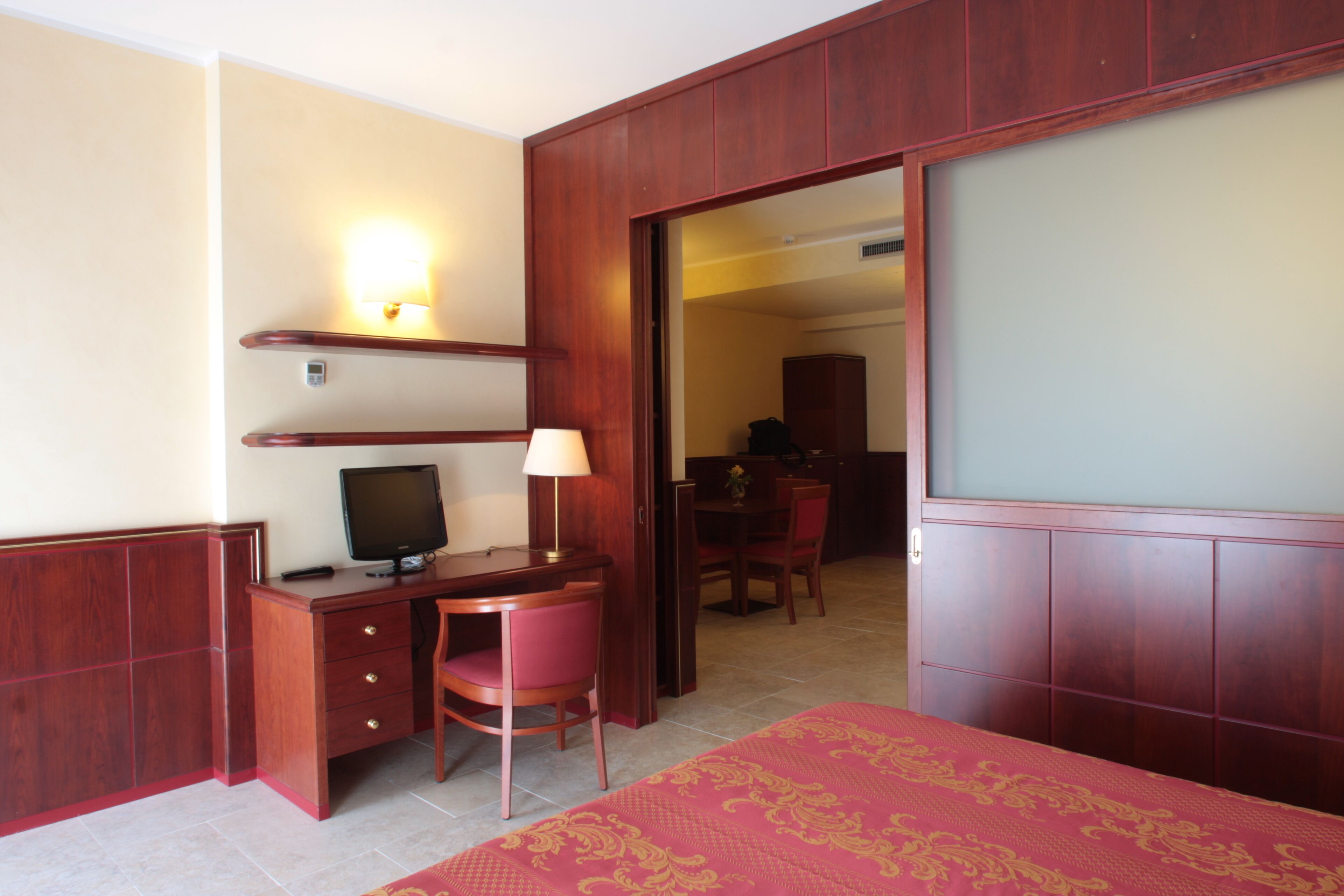 A hotel room with a wooden desk, a television, a chair, and a bed with a patterned bedspread.
