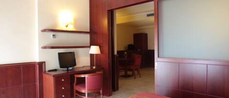 A hotel room with a wooden desk, a television, a chair, and a bed with a patterned bedspread.