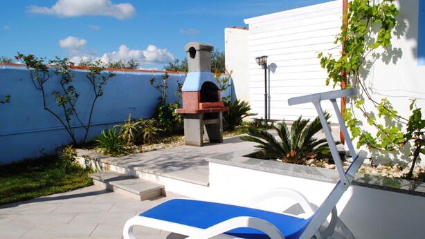 A patio with a blue lounge chair, a barbecue grill, and a white wall in the background.