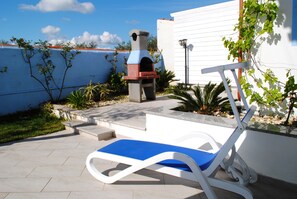 A patio with a blue lounge chair, a barbecue grill, and a white wall in the background.