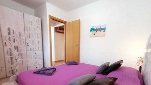 A bedroom with a bed, pillows, a wardrobe, and a painting on the wall.