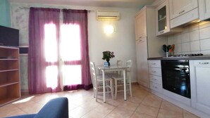 A compact kitchen with white cabinets, a dining table with chairs, and a blue sofa.