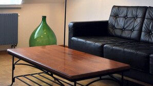 A modern living room with a wooden coffee table, a black floor lamp, a green vase, and a black leather sofa. - Guesthouse fürDich (Zürich)
