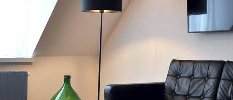 A modern living room with a wooden coffee table, a black floor lamp, a green vase, and a black leather sofa.