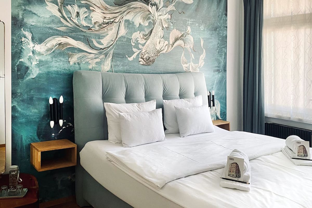 A bedroom with a large bed, a headboard, bedside tables, and a wall mural.
