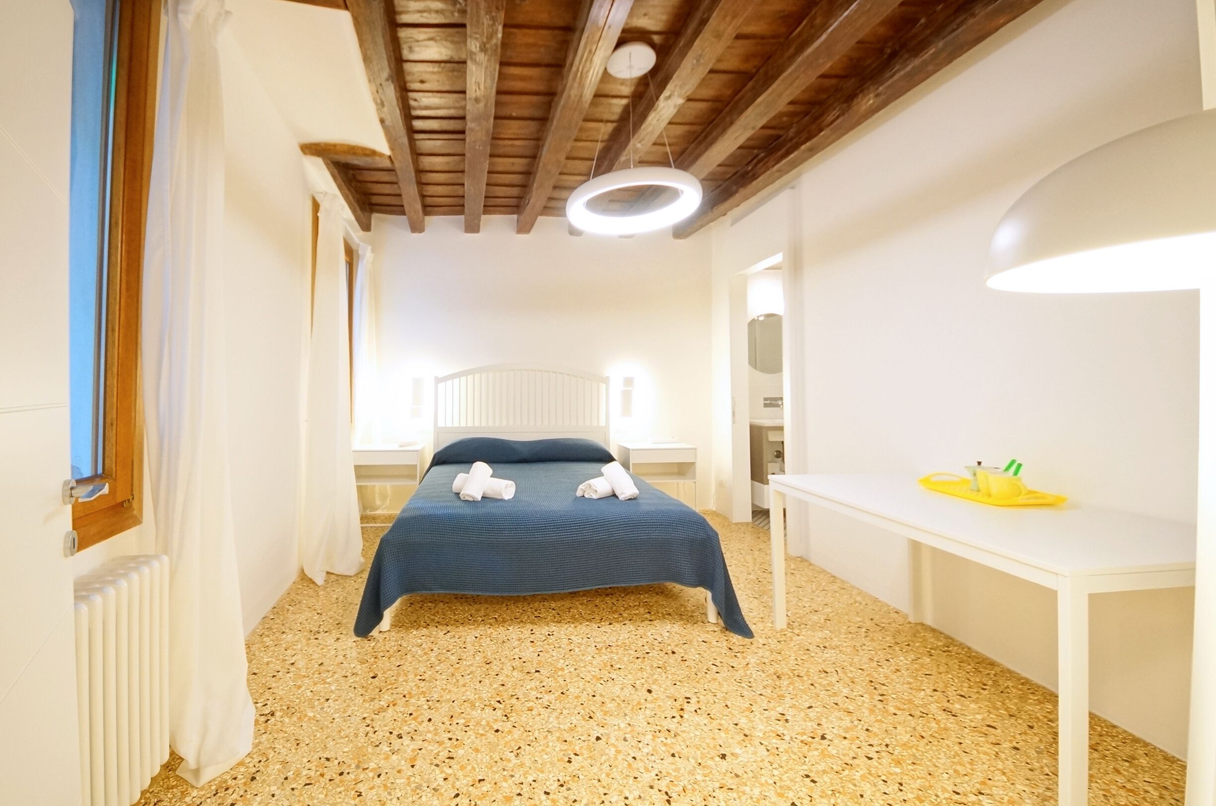 Une chambre à coucher avec un lit, un bureau blanc et un luminaire fixé au plafond.