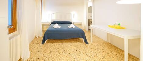 Une chambre à coucher avec un lit, un bureau blanc et un luminaire fixé au plafond.