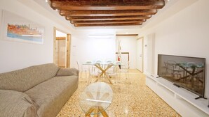 Un salon moderne avec une table basse en verre, un canapé, un téléviseur posé sur un meuble et un coin repas comprenant une table et des chaises en verre.