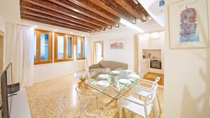 Un espace repas avec une table en verre, des chaises blanches et un plafond en bois.
