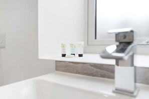 Un baño con un lavamanos blanco, un espejo y tres botellas de artículos de tocador en la encimera.