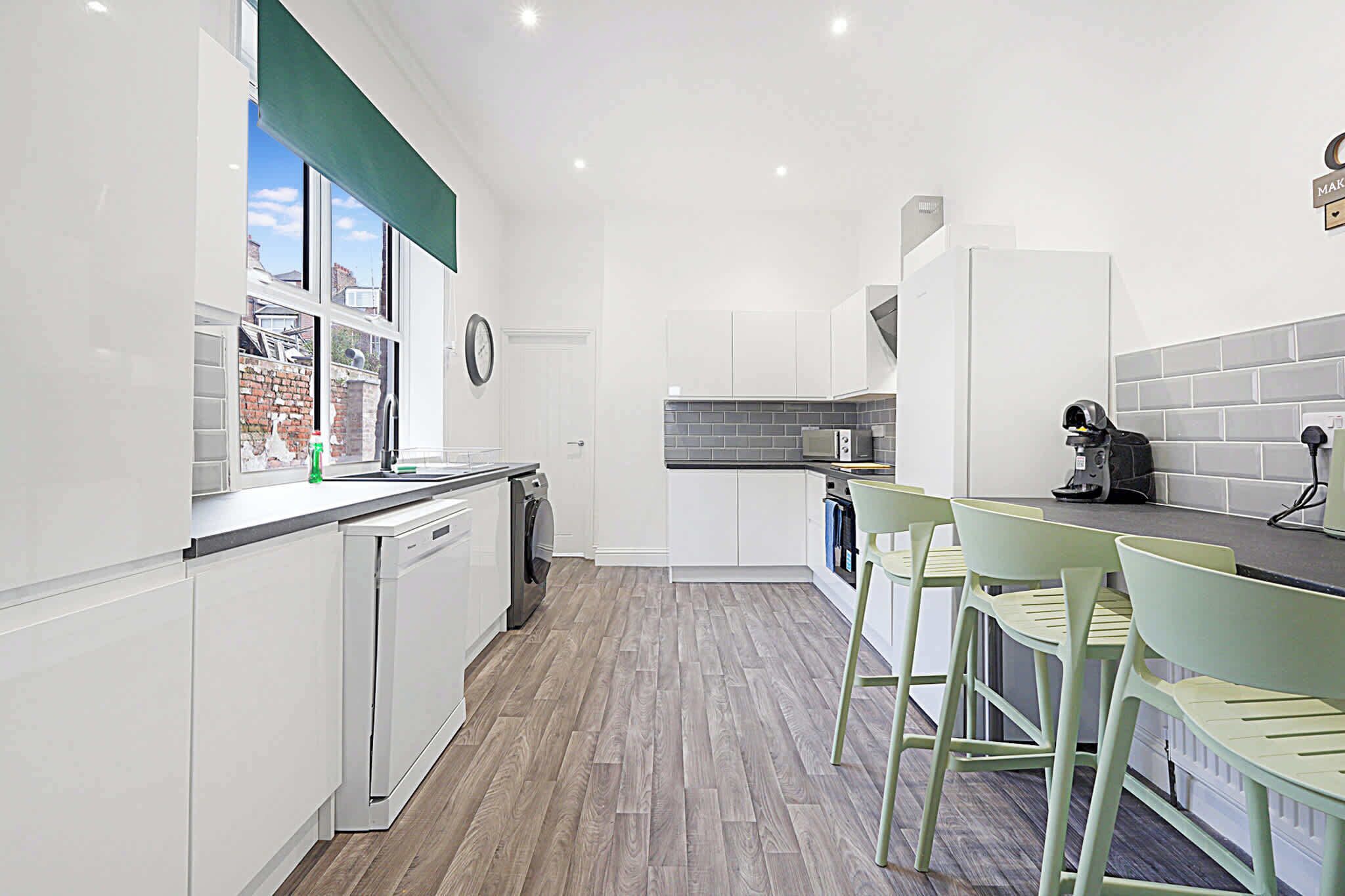 A modern kitchen with white cabinets, a wooden floor, and a view of the outside through a window.