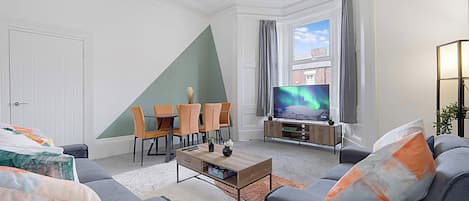 A modern living room with a dining area, a television, and a view of the sky.