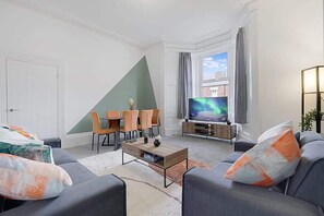 Una sala de estar con televisor, sofá y sillones.