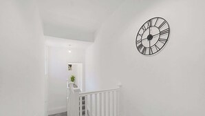 Una escalera con barandilla blanca que lleva a una plataforma, una pared blanca y un reloj grande.