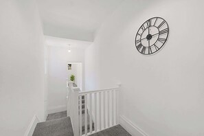 Una escalera con barandilla blanca que lleva a una plataforma, una pared blanca y un reloj grande.