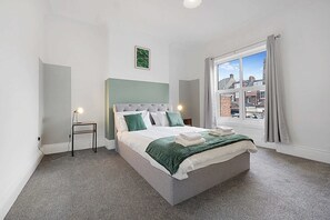 Un dormitori amb un llit, una nitòria, una finestra amb cortines i vista a edificis a l'exterior.