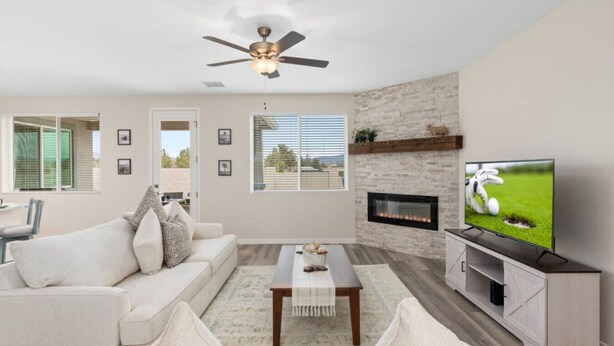 A modern living room with a fireplace, a flat-screen TV, a ceiling fan, and a large window.