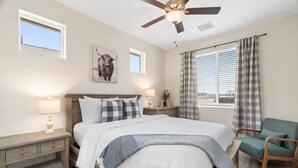 A bedroom with a bed, a nightstand, a chair, a ceiling fan, and a window with curtains.