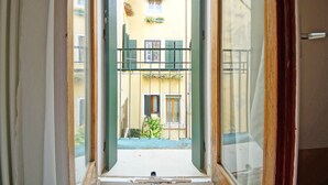 Une porte ouverte donne sur une cour intérieure agrémentée d’un balcon, d’un petit jardin et d’un bâtiment à la façade jaune.