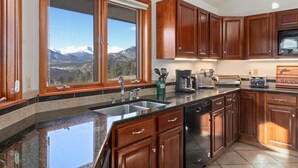 Una cocina con armarios de madera, encimera de granito, lavavajillas y vistas a montañas a través de un ventanal.