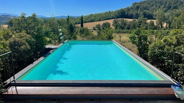 A rectangular swimming pool with a clear blue water surface, surrounded by lush greenery and hills in the background. - Adam House, exclusive Pool, outstanding views, vast garden, aircon, sleeps 8 (Provincia di Perugia)