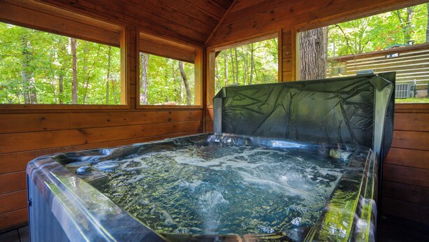A hot tub in a wooden cabin with large windows overlooking a forest. - Scenic Hideaway: Pet-Friendly, Secluded, Game Room, fire pit, hot tub, Wi-Fi (Sevierville)