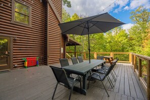 A wooden deck with a table and chairs, an umbrella, and a view of trees.