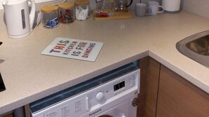 Eine kleine Küche mit Waschmaschine, Kaffeemaschine und einem Schild, das darauf hinweist, dass die Küche zum Tanzen gedacht ist.