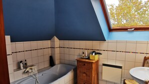 A bathroom with a bathtub, toilet, vanity, and a window with a view of trees. - Studio Spacieux, Route des Vins (Rosheim)