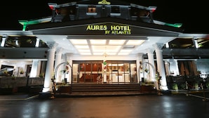The exterior of Aures Hotel by Atlantis at night, featuring a grand entrance with steps, a large chandelier, and decorative columns. - AURES HOTEL BY ATLANTIS (Akbou)
