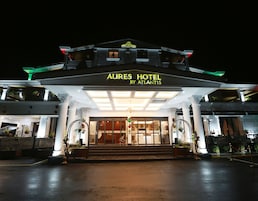 El exterior del Hotel Aures by Atlantis de noche, con una entrada imponente que incluye escalones, una lámpara de araña grande y columnas decorativas.
