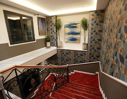 Una escalera con alfombra roja, barandilla de metal y un muro con diseños geométricos.