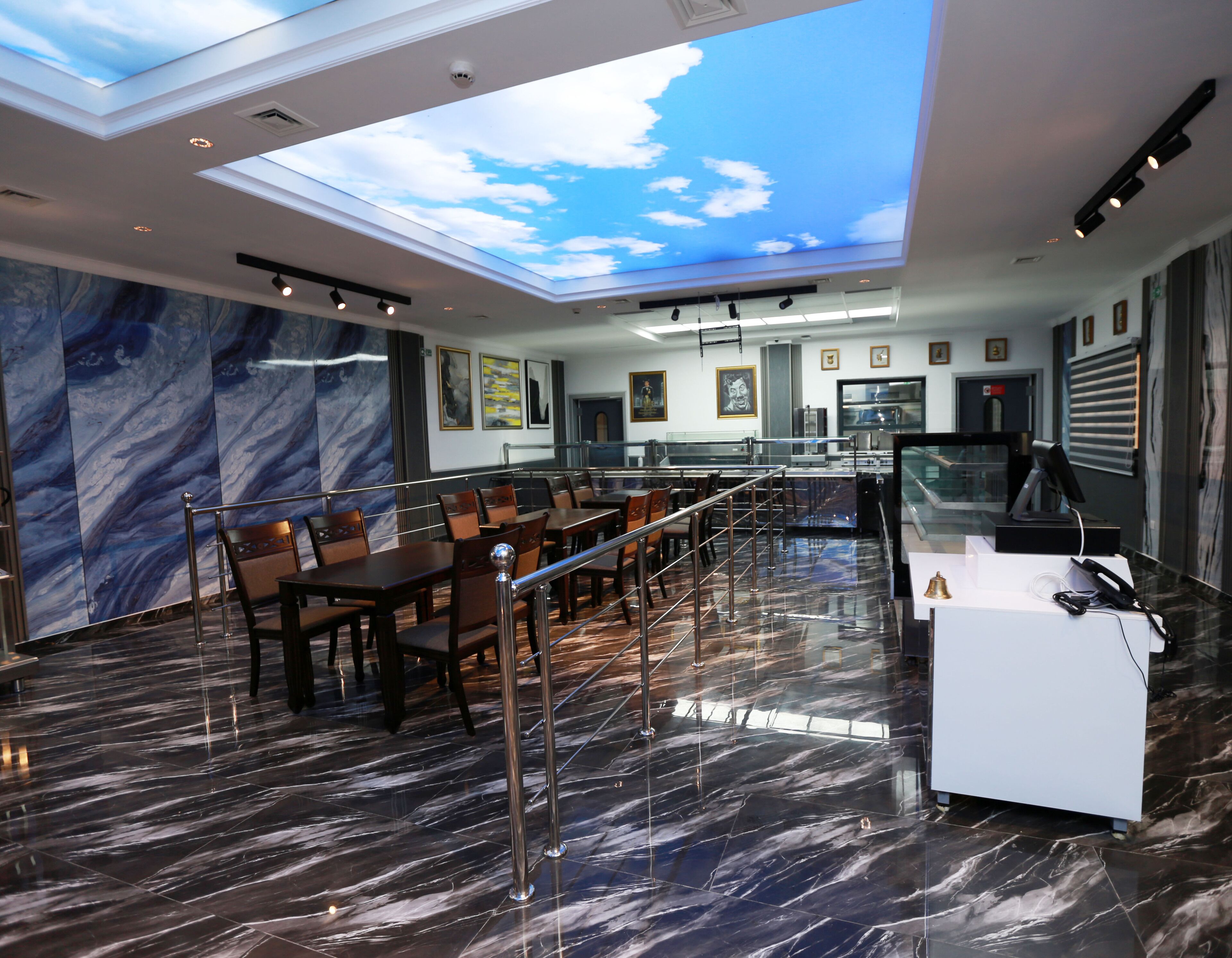A modern restaurant with a high ceiling, marble flooring, and a view of the sky through a skylight.